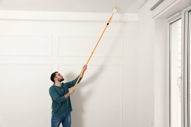 Photo of Young man painting ceiling with white dye indoors, space for text