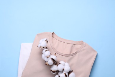 Photo of Cotton branch with fluffy flowers and t-shirts on light blue background, top view. Space for text