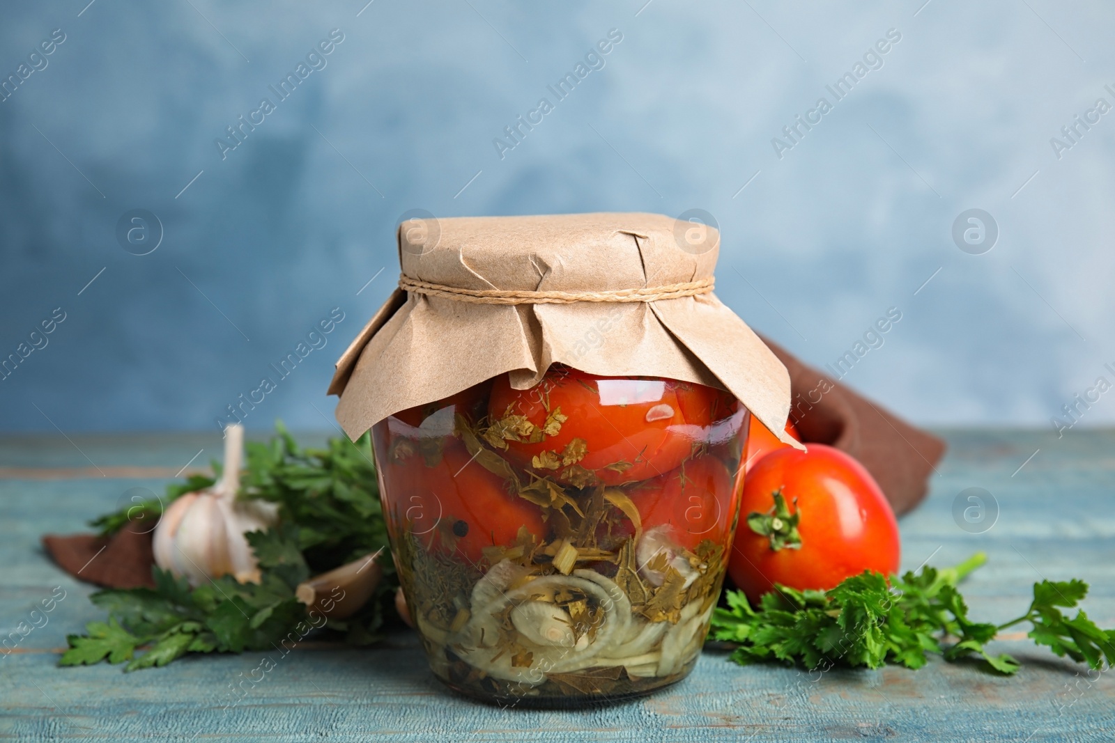 Photo of Pickled tomatoes in glass jar and products on blue wooden table