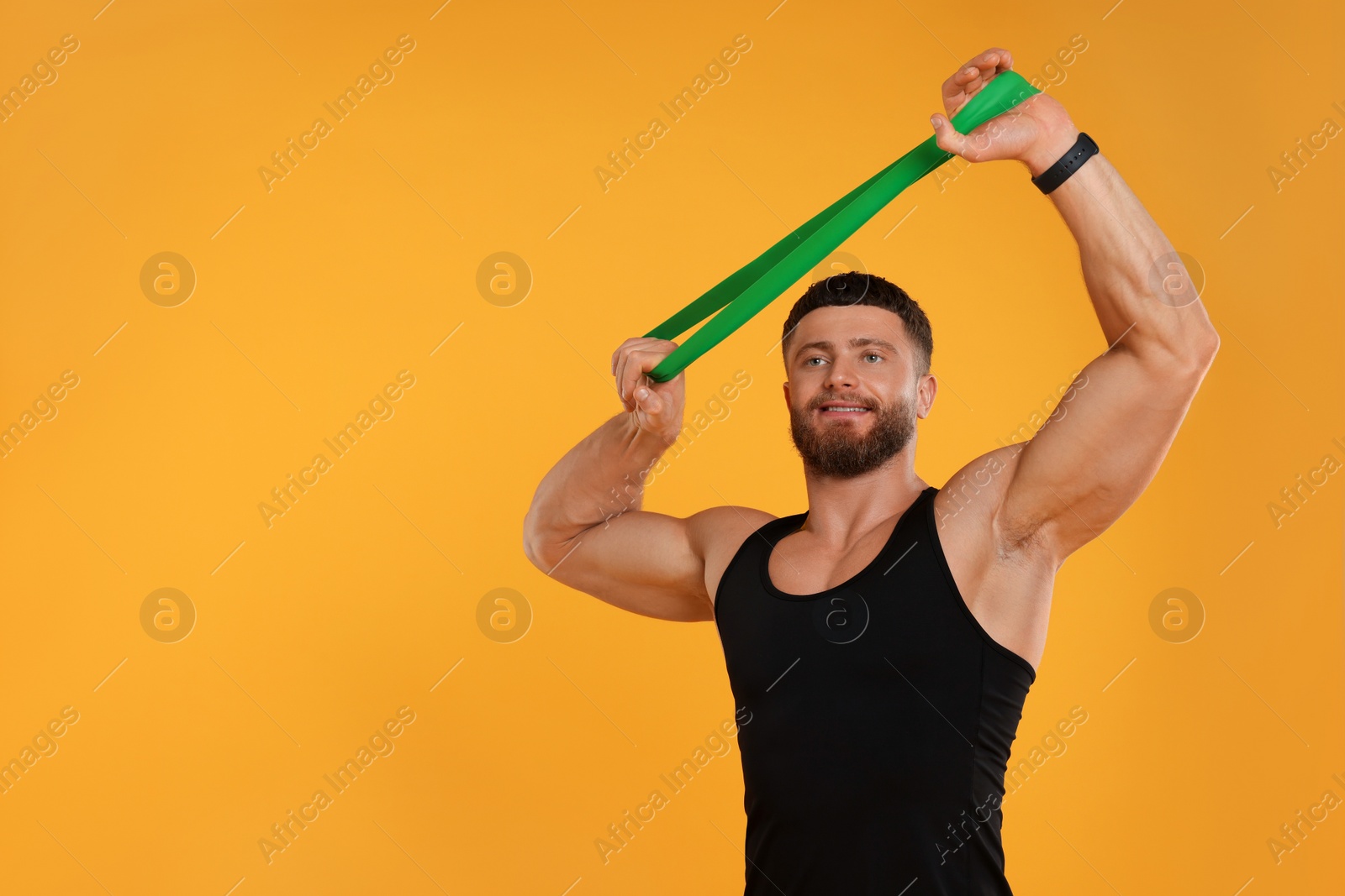 Photo of Young man exercising with elastic resistance band on orange background. Space for text