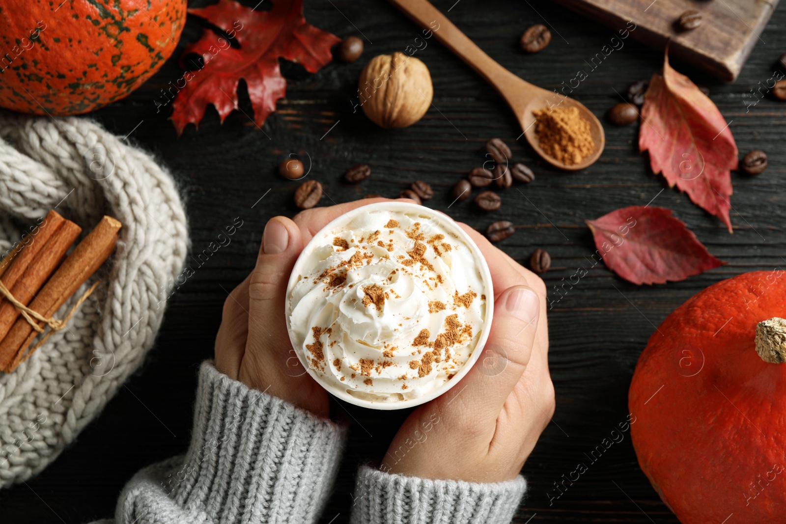 Photo of Woman holding cup with tasty pumpkin spice latte at black wooden table, closeup