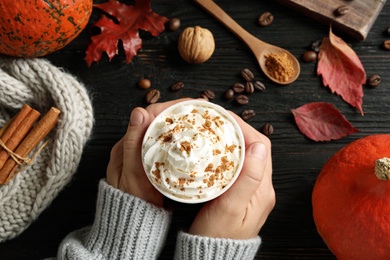 Woman holding cup with tasty pumpkin spice latte at black wooden table, closeup
