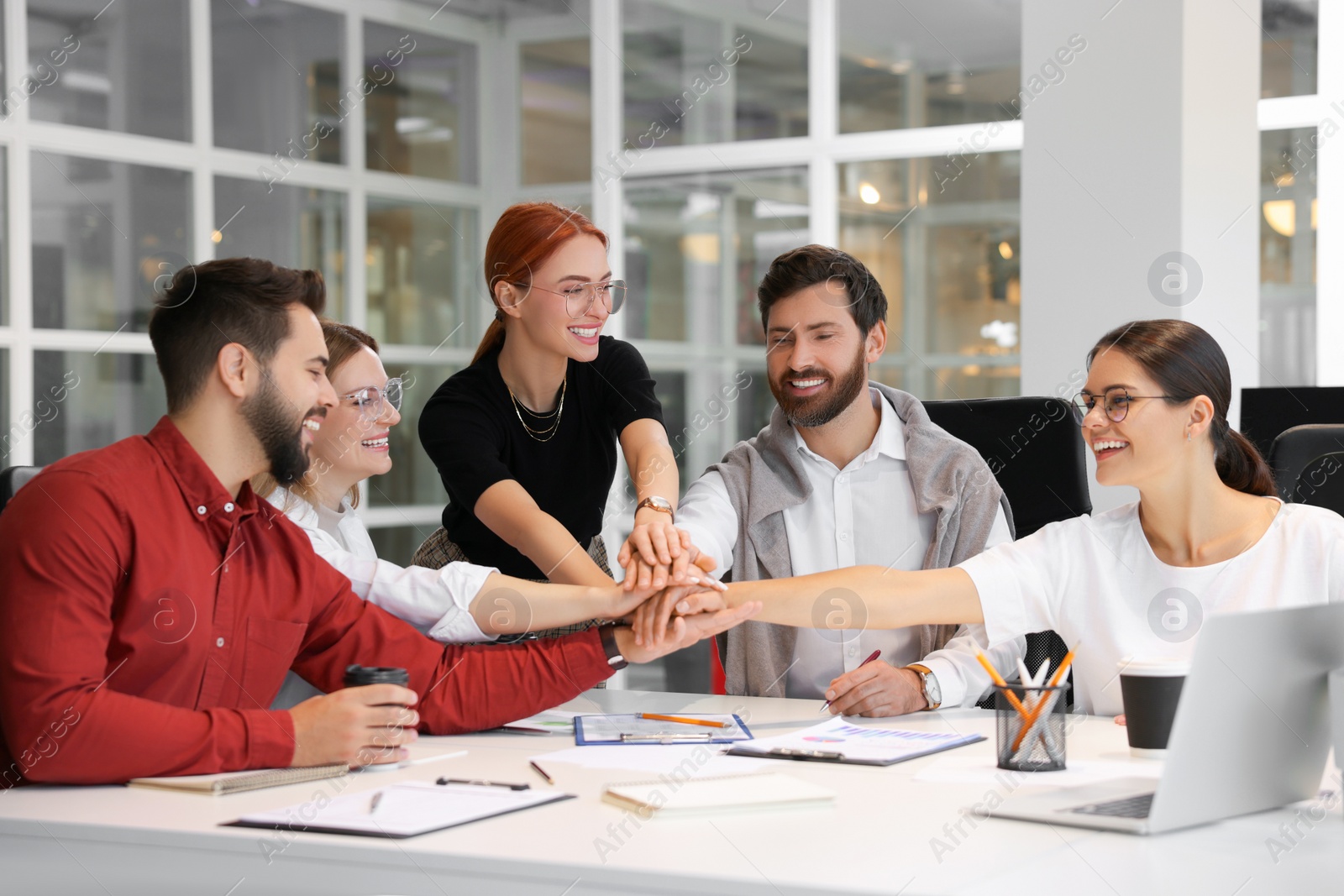 Photo of Team of employees joining hands in office