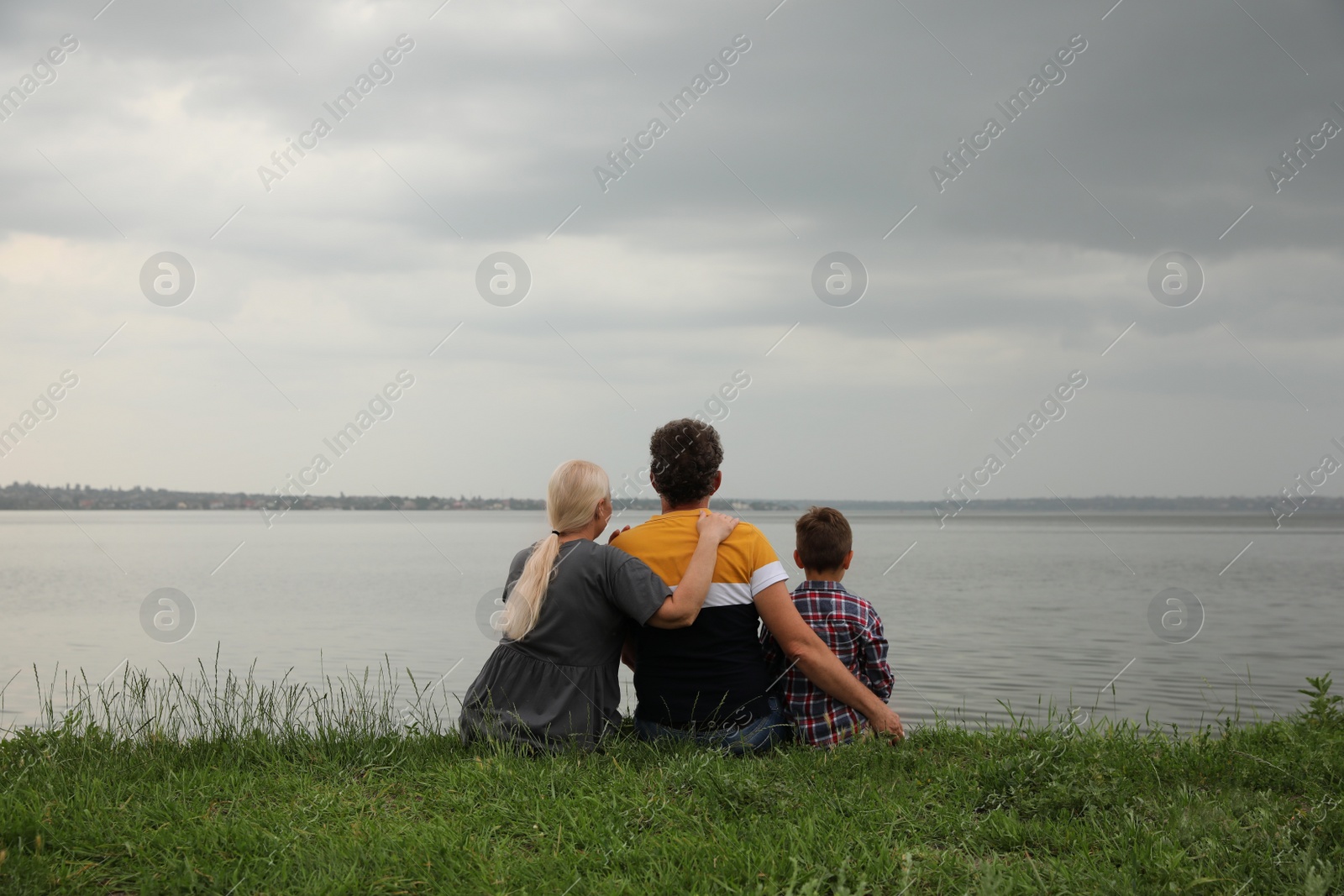 Photo of Cute little boy and grandparents spending time together near river, back view