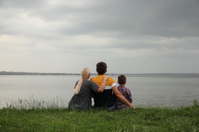 Photo of Cute little boy and grandparents spending time together near river, back view