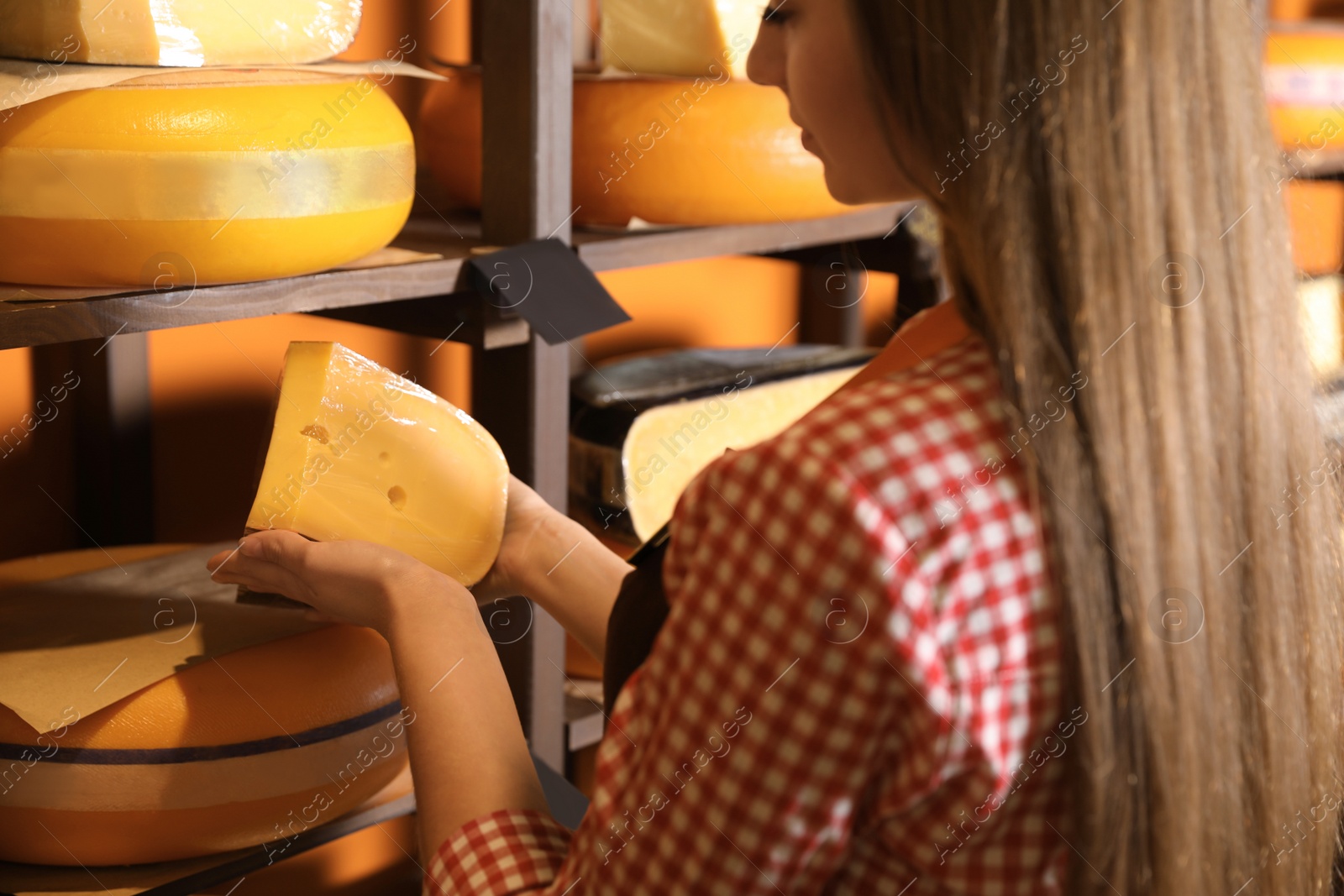 Photo of Seller with piece of delicious cheese near rack in store