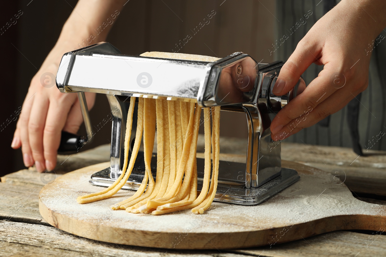 Photo of Woman making homemade noodles with pasta maker at wooden table, closeup
