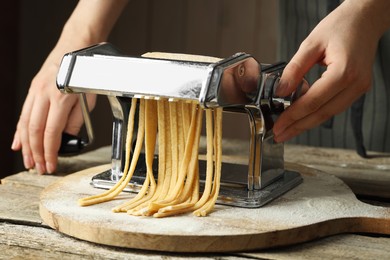 Photo of Woman making homemade noodles with pasta maker at wooden table, closeup