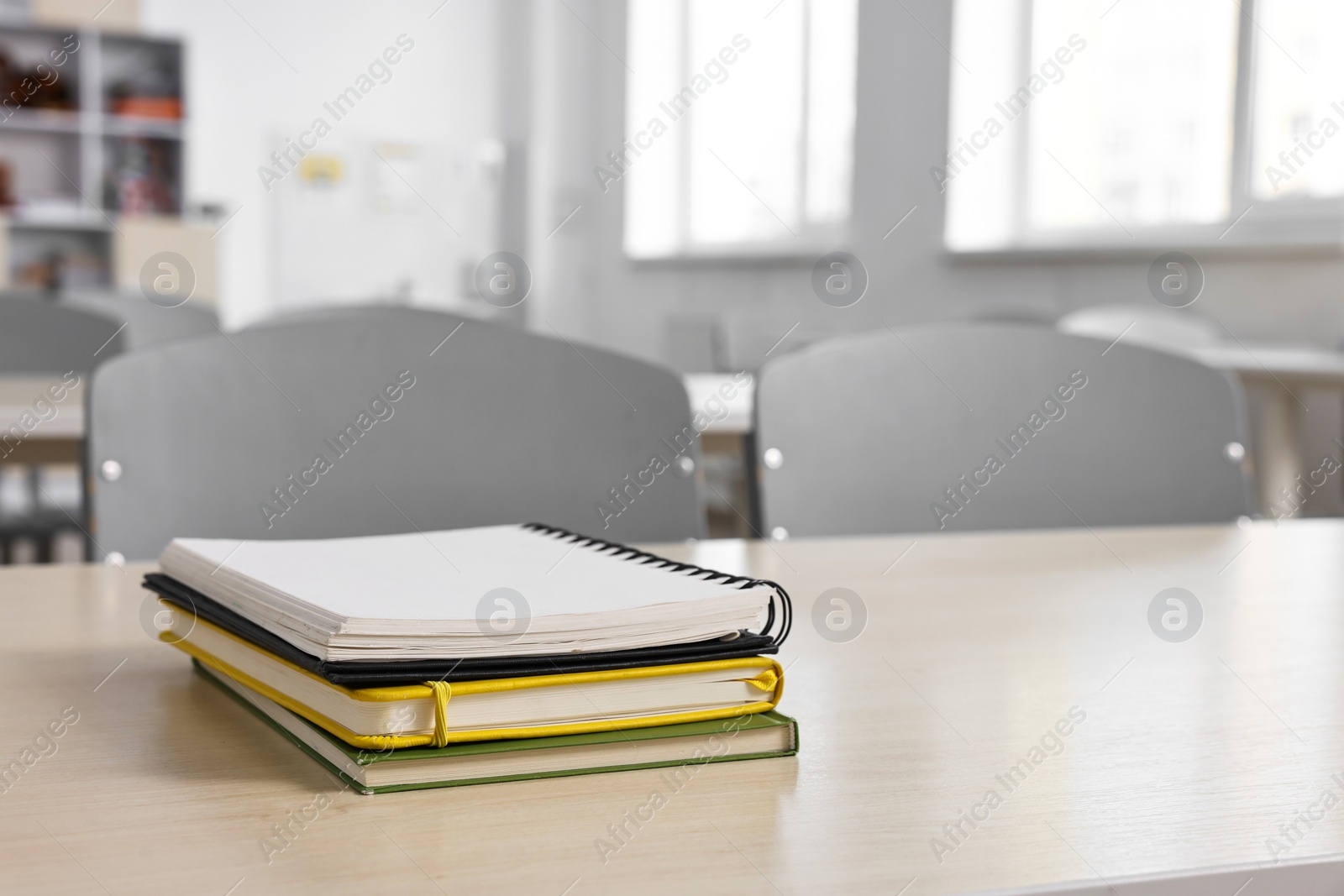 Photo of Stack of notebooks on wooden desk in empty classroom