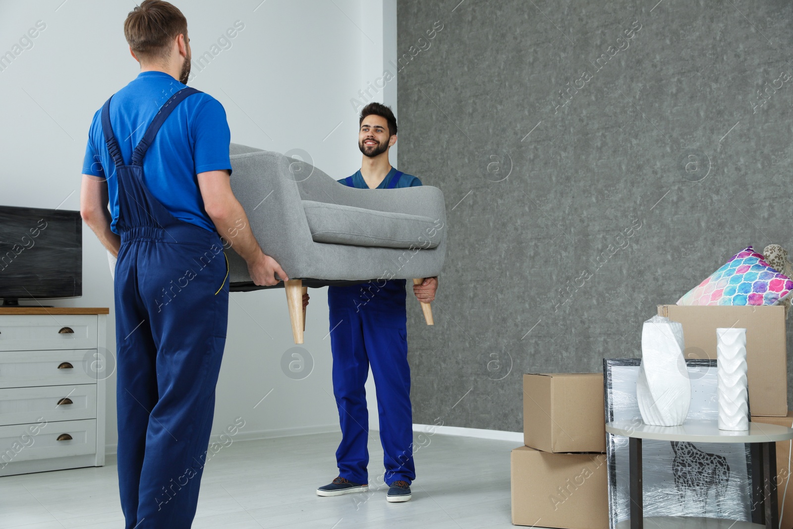 Photo of Young workers carrying sofa in room. Moving service