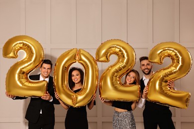 Photo of Happy friends with golden 2022 balloons indoors. New Year celebration