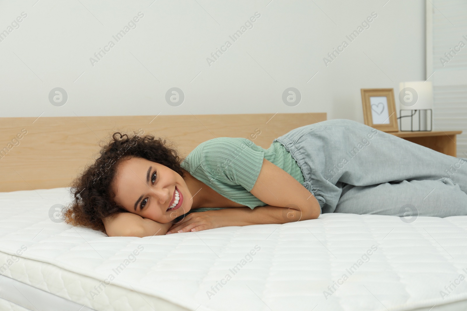 Photo of Happy young African American woman on bed with comfortable mattress at home