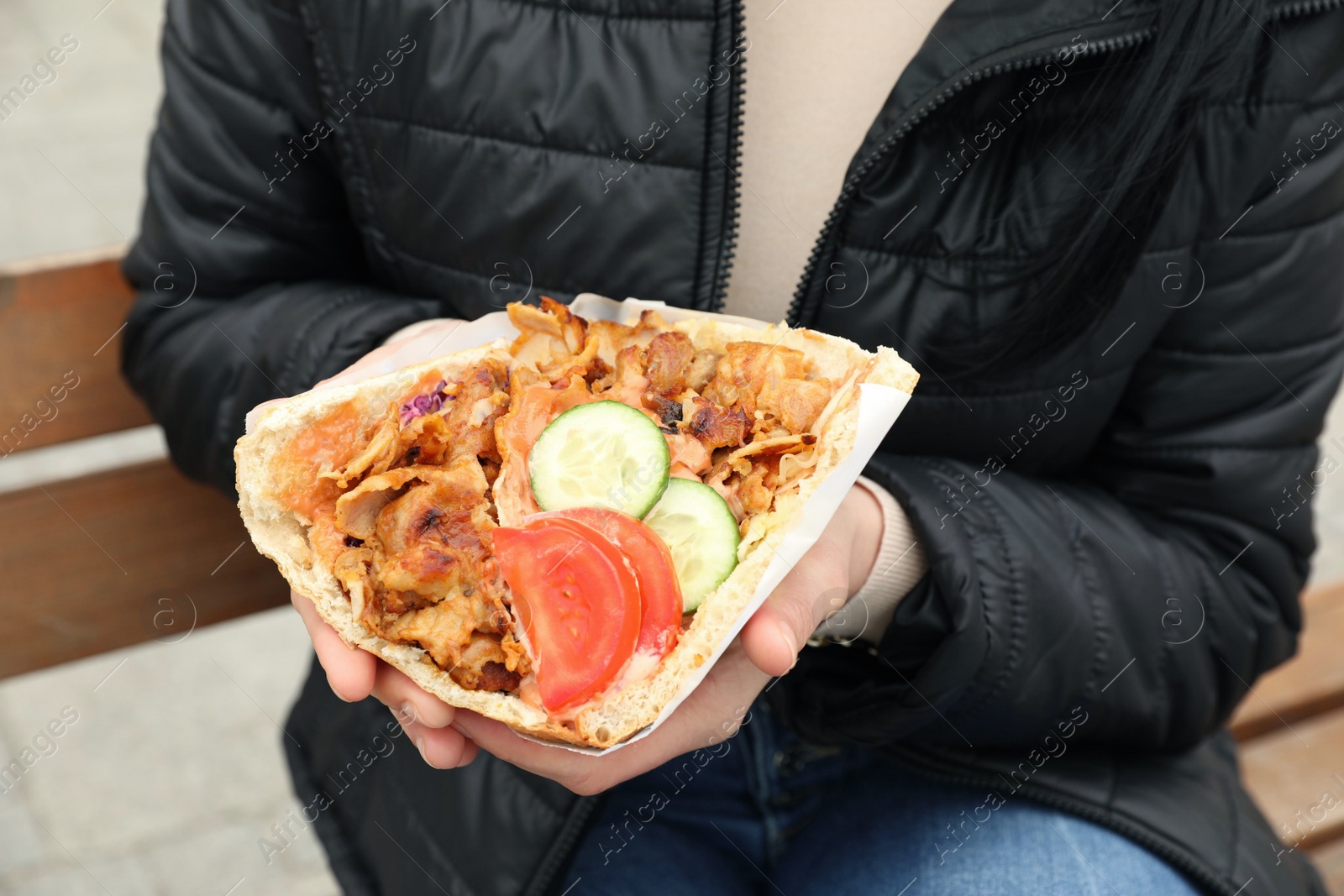 Photo of Woman holding delicious bread with roasted meat and vegetables outdoors, closeup. Street food