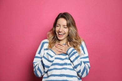 Cheerful young woman laughing on pink background