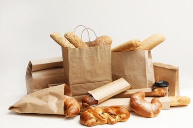 Different fresh bakery products in paper bags on white background