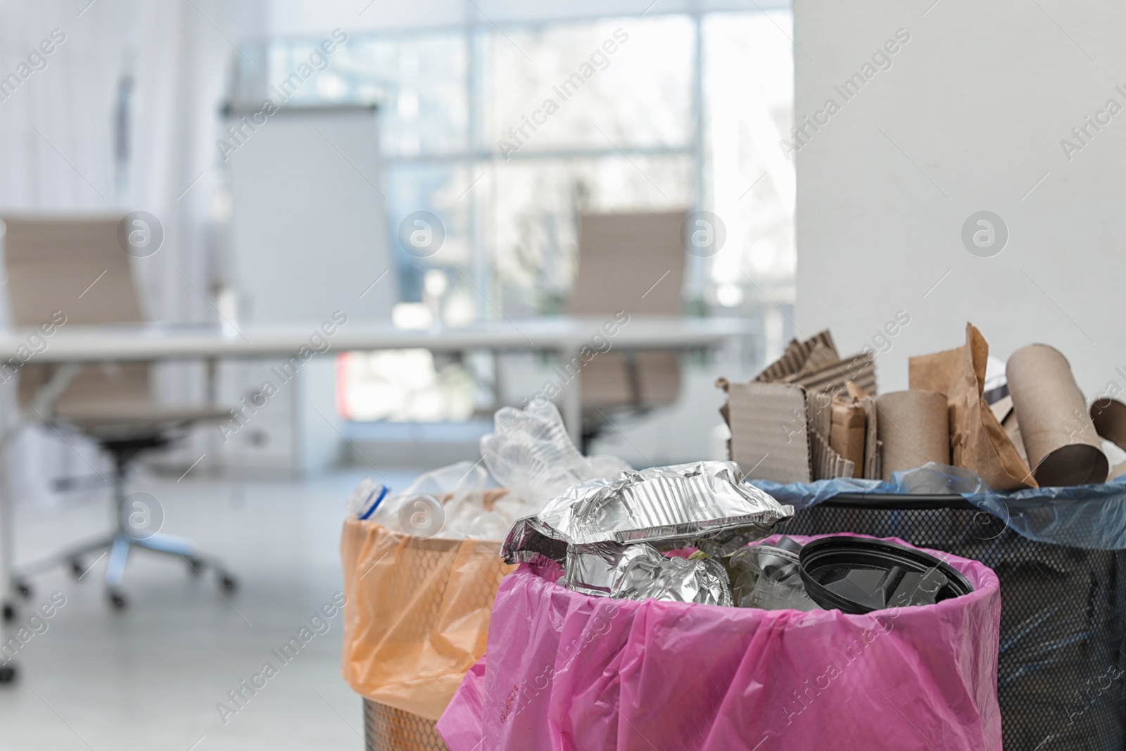 Photo of Full trash cans in modern office, space for text. Waste recycling