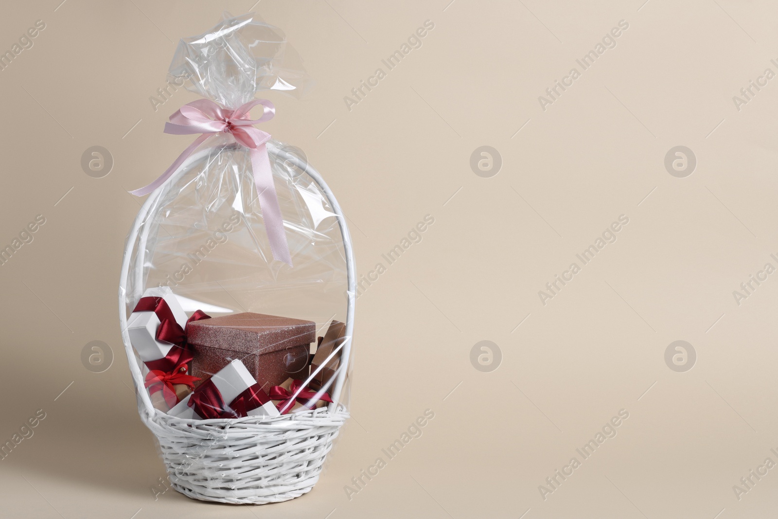 Photo of Wicker basket full of gift boxes on beige background. Space for text