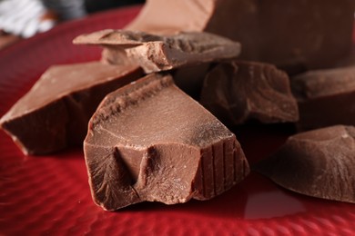 Photo of Pieces of tasty milk chocolate on red plate, closeup