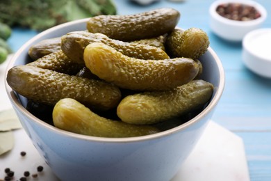 Photo of Bowl with pickled cucumbers on light blue table, closeup