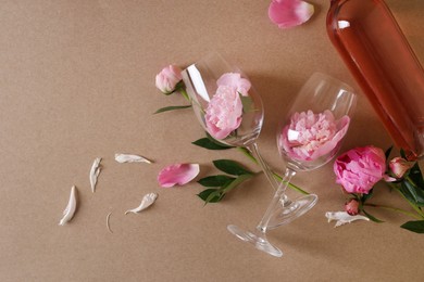 Photo of Bottle of rose wine, glasses and beautiful pink peonies on brown background, flat lay