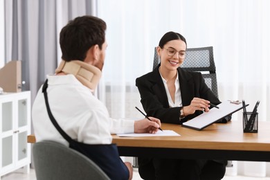 Injured man signing document in lawyer's office, selective focus