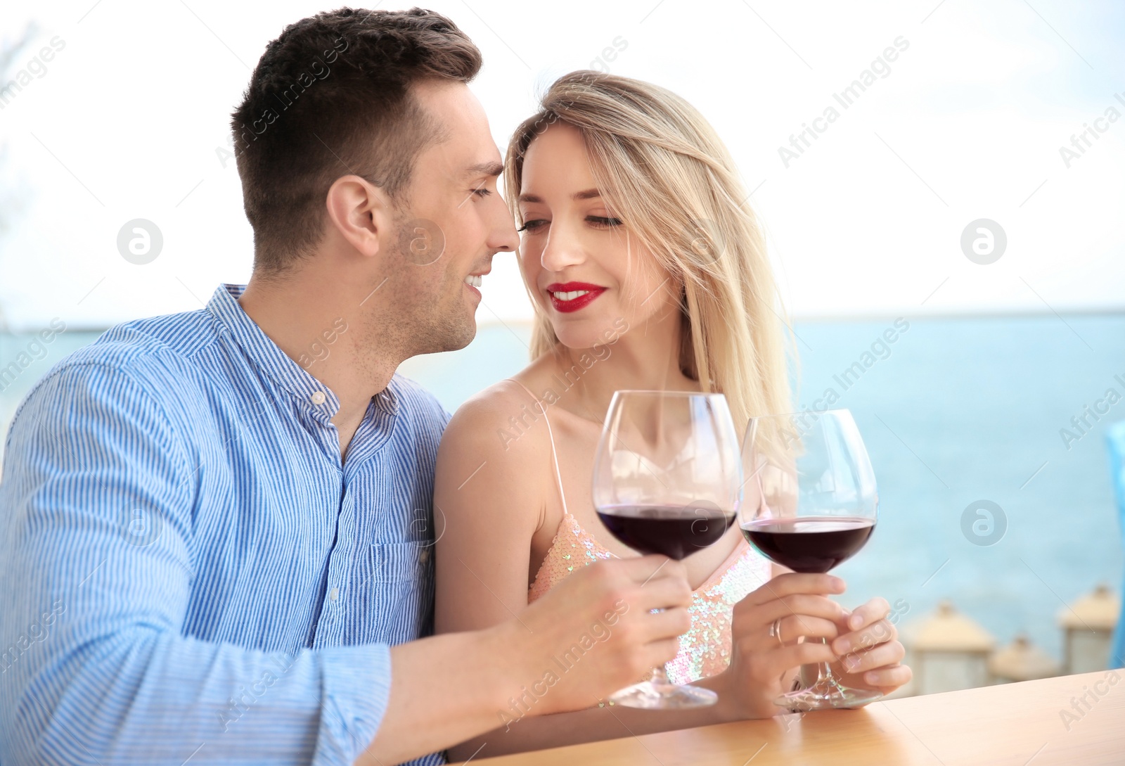 Photo of Young romantic couple with glasses of red wine at table