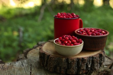 Dishes with tasty wild strawberries on stump against blurred background, closeup. Space for text