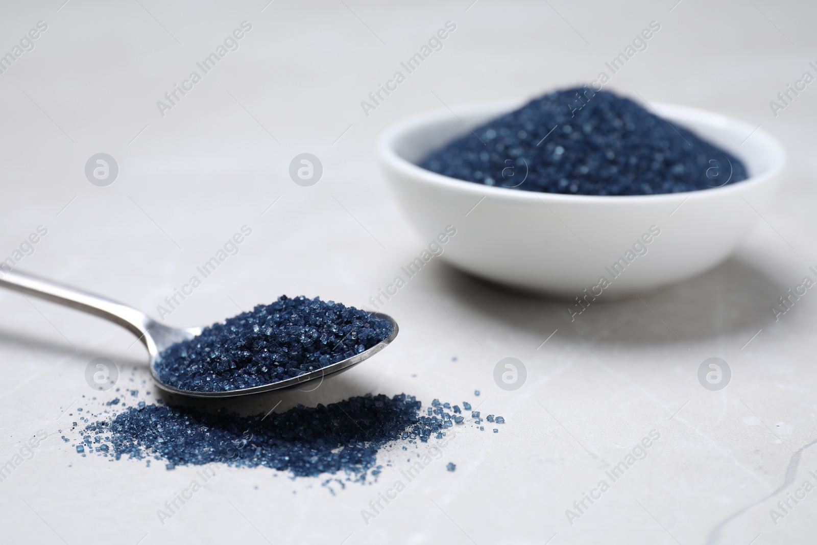 Photo of Bowl and spoon with blue food coloring on light grey table. Space for text