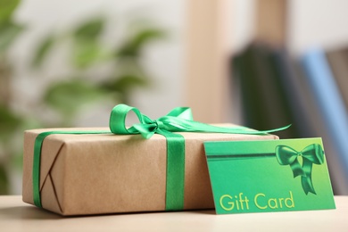 Photo of Gift card and present on table against blurred background, space for text