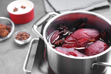 Photo of Tasty red wine poached pears and spices in pot on grey table, closeup