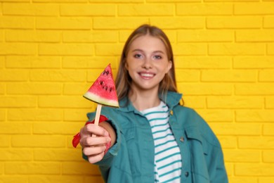 Photo of Beautiful girl with piece of watermelon near yellow brick wall, focus on hand