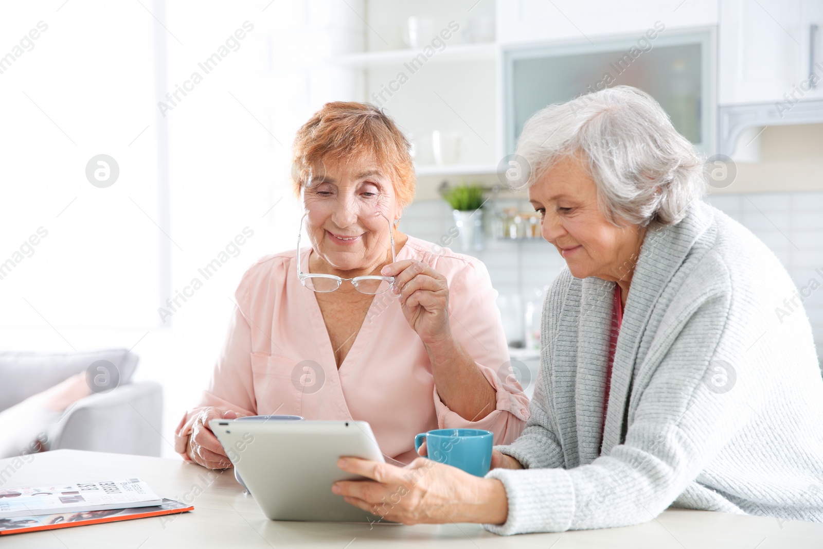 Photo of Elderly women using tablet PC at table in kitchen