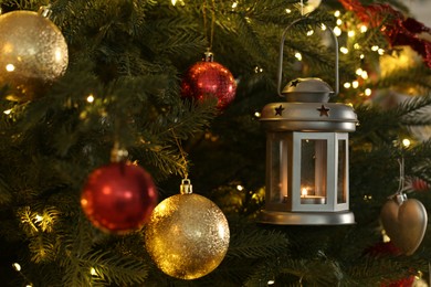 Photo of Christmas lantern with burning candle and balls on fir tree as background, closeup