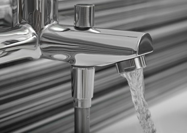 Photo of Water flowing from bath tap on blurred background, closeup