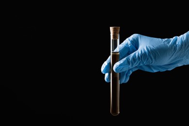Photo of Scientist holding test tube with liquid on black background, closeup. Space for text