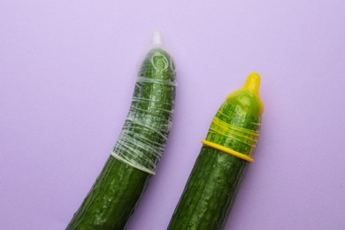 Photo of Cucumbers with condoms on lilac background, flat lay. Safe sex concept