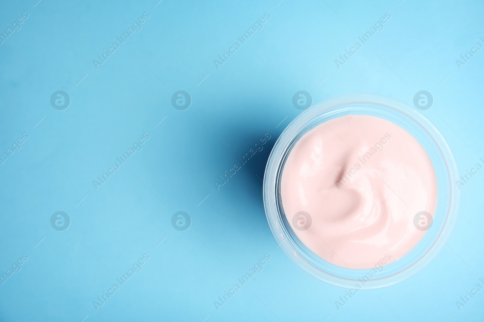 Photo of Plastic cup with creamy yogurt and space for text on color background, top view