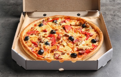 Photo of Cardboard box with delicious pizza on table