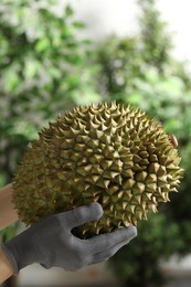 Photo of Woman in gloves holding fresh ripe durian outdoors, closeup