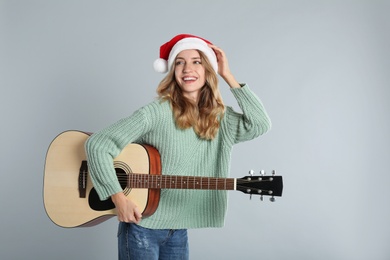 Photo of Young woman in Santa hat with acoustic guitar on light grey background. Christmas music