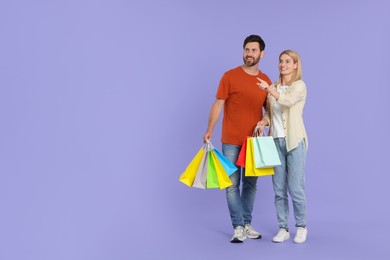 Family shopping. Happy couple with many colorful bags on violet background. Space for text