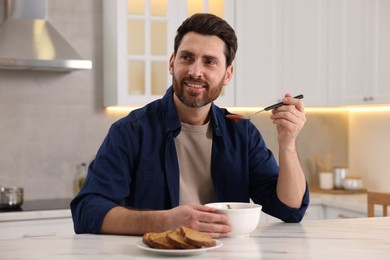 Photo of Man eating delicious tomato soup at light marble table in kitchen