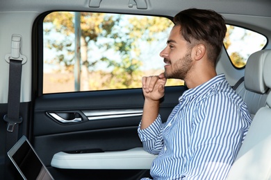 Photo of Young handsome man with laptop in back seat of car