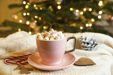 Cup of tasty cocoa with marshmallows, candy canes and Christmas decor on knitted plaid indoors