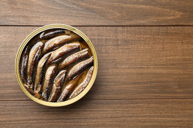 Photo of Sprats in tin can on wooden table, top view. Space for text