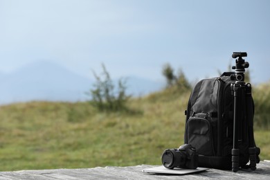 Photo of Photographer's backpack, camera, tripod and laptop on wooden surface outdoors. Space for text