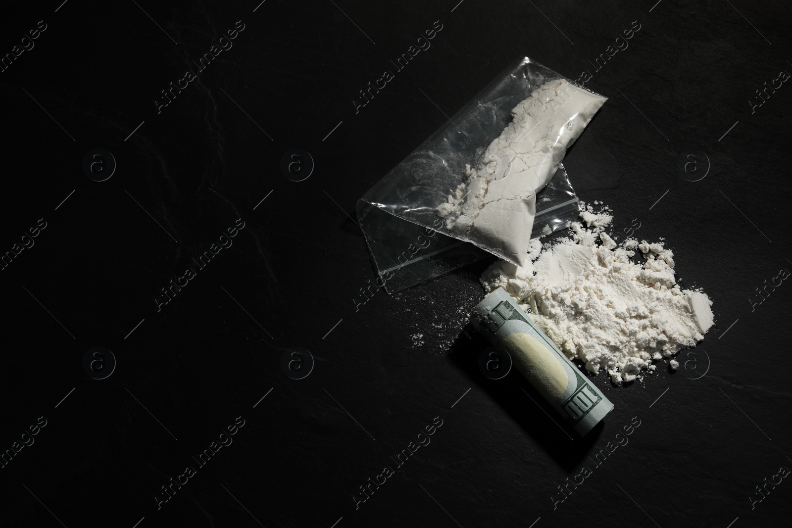 Photo of Plastic bag with hard drug and rolled dollar banknote on dark textured background, flat lay. Space for text