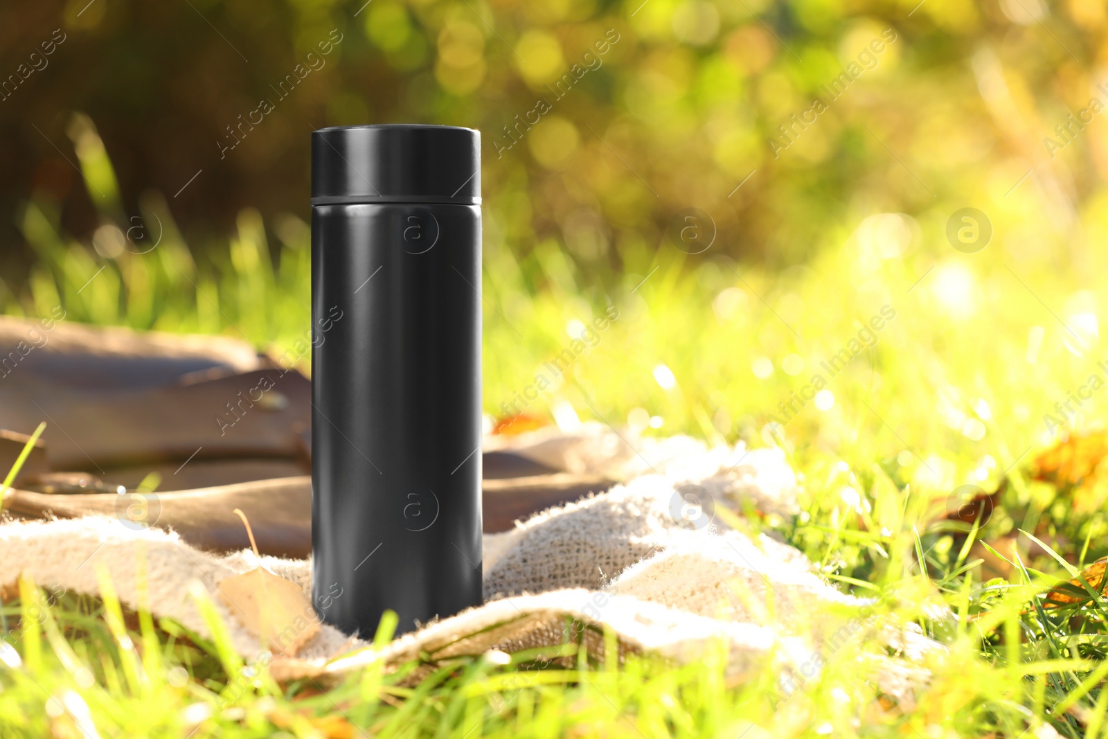 Photo of Black thermos and blanket on green grass outdoors, space for text