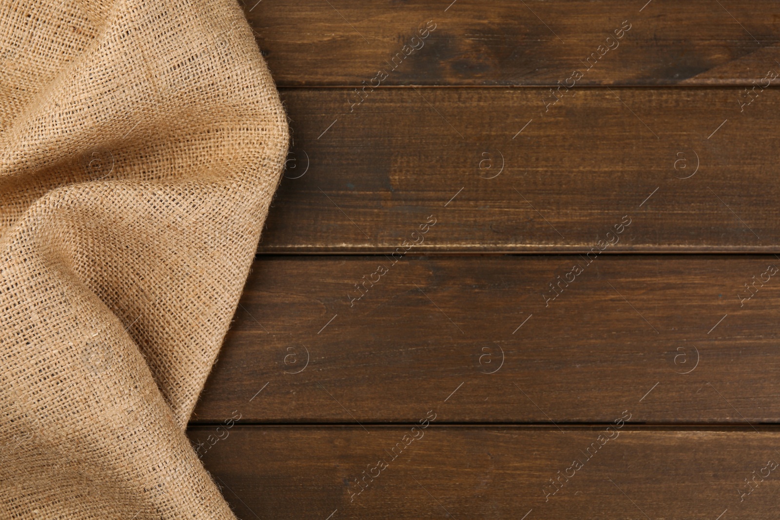 Photo of Brown burlap fabric on wooden table, top view. Space for text