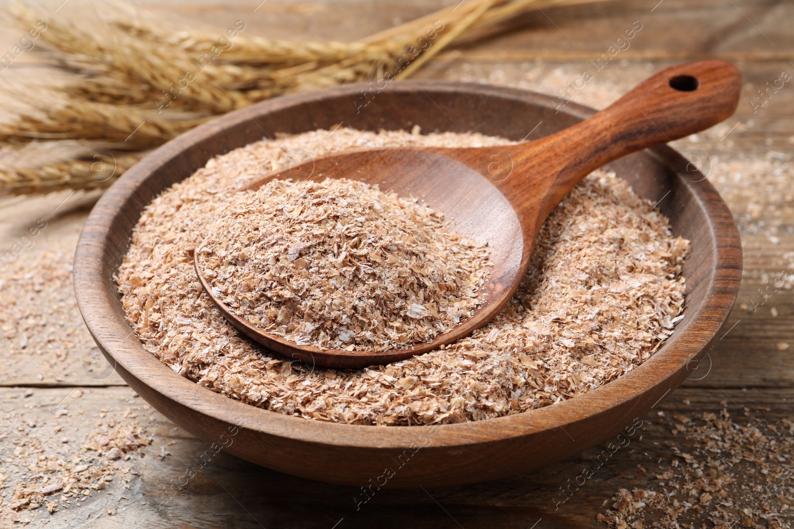 Photo of Wheat bran and spoon in bowl on wooden table